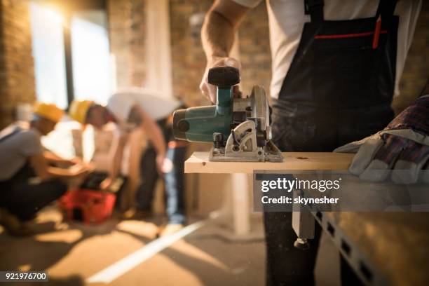 unrecognizable worker cutting plank with circular saw at construction site. - residential construction stock pictures, royalty-free photos & images