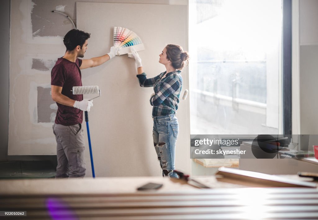 Young couple choosing the right color for their wall while renovating apartment.