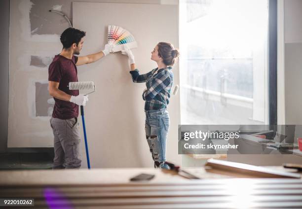 young couple choosing the right color for their wall while renovating apartment. - house paint sample stock pictures, royalty-free photos & images