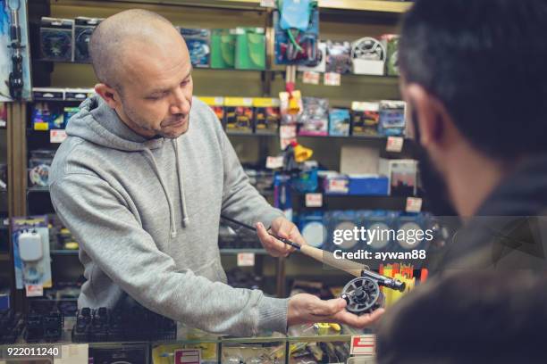 young man buying fishing rod in a store - barbed hook stock pictures, royalty-free photos & images