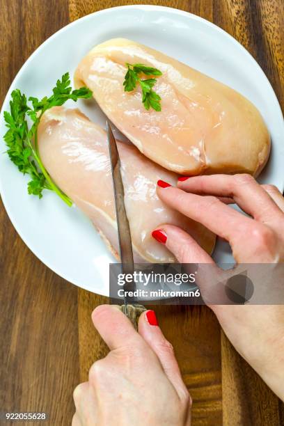 cropped hand of woman cutting raw chicken breast. - hoja de aluminio fotografías e imágenes de stock