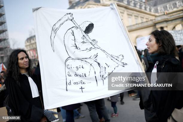 Two women hold a placard reading on a gravestone "here lies the asylum right" during a gather called by the French Office for Refugees and Stateless...