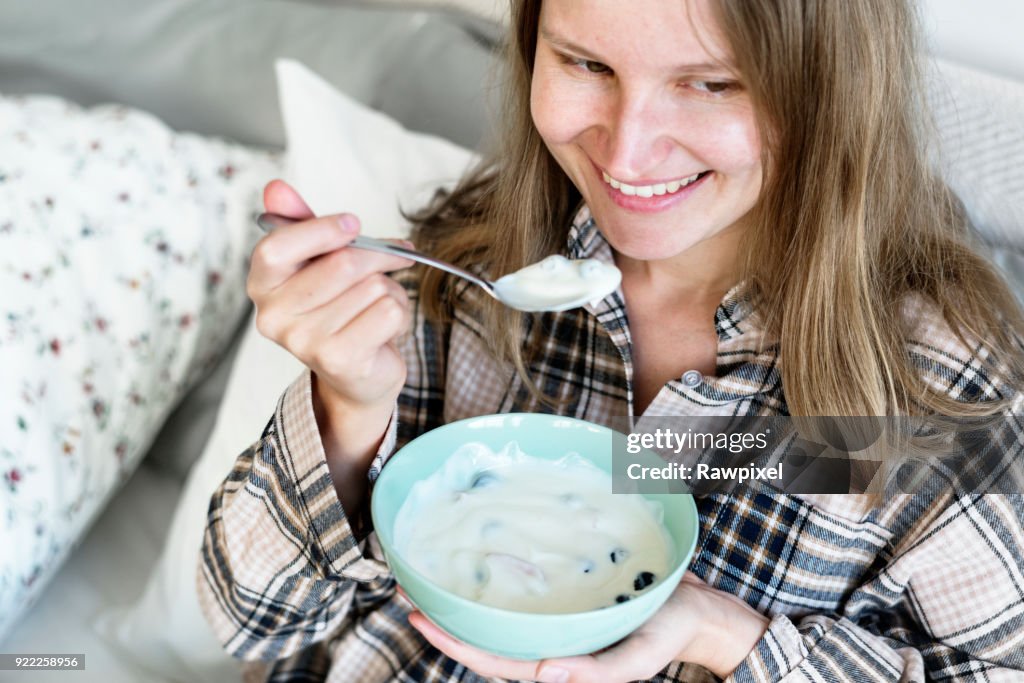 Caucasian girl eating yogurt on bed