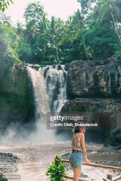 woman looking at tegenungan waterfall in tropical forest in bali - rainy season stock pictures, royalty-free photos & images