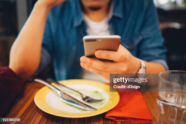 close up of young man using mobile phone while having meal in a restaurant - dinner program stock pictures, royalty-free photos & images