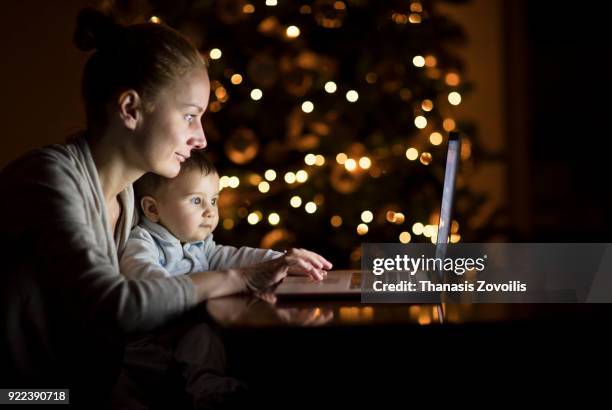 mother with her baby looking a laptop in the dark - thanasis zovoilis stock pictures, royalty-free photos & images