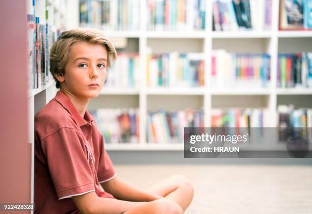 portrait of schoolboy sitting in library - one boy only stock pictures, royalty-free photos & images