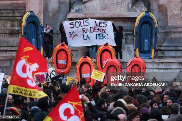 Protesters hold a banner reading "Under the rafts, the sea" as they stand next to inflatable dinghies on the Place Saint-Michel in Paris on February...