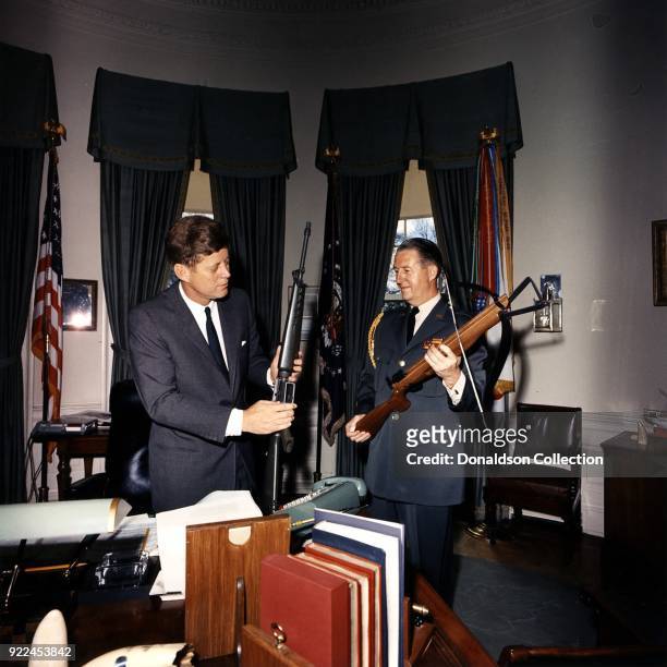 President Kennedy examining an early Colt AR-15 in the White House Oval Office, April 19, 1963. His aide, Major General "Ted" Clifton, is holding an...