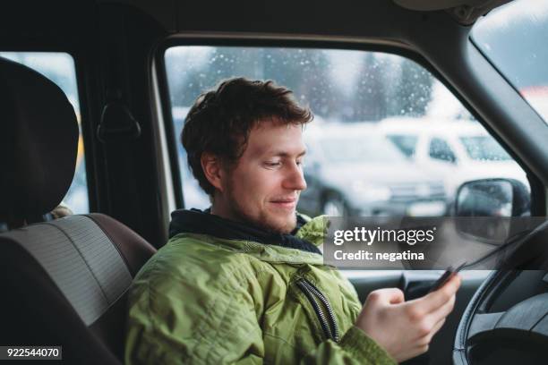 portrait of young smiling man in the green jacket holding smartphone in the car - grüne jacke stock-fotos und bilder