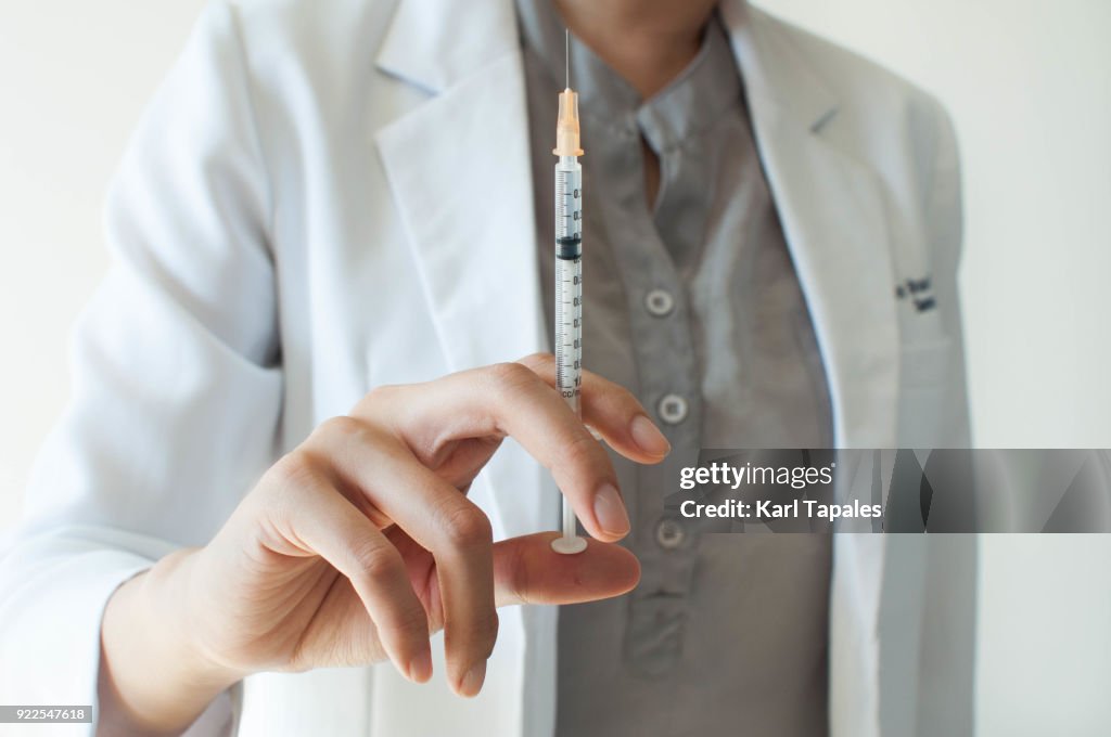 A female doctor in white coat is holding a syringe