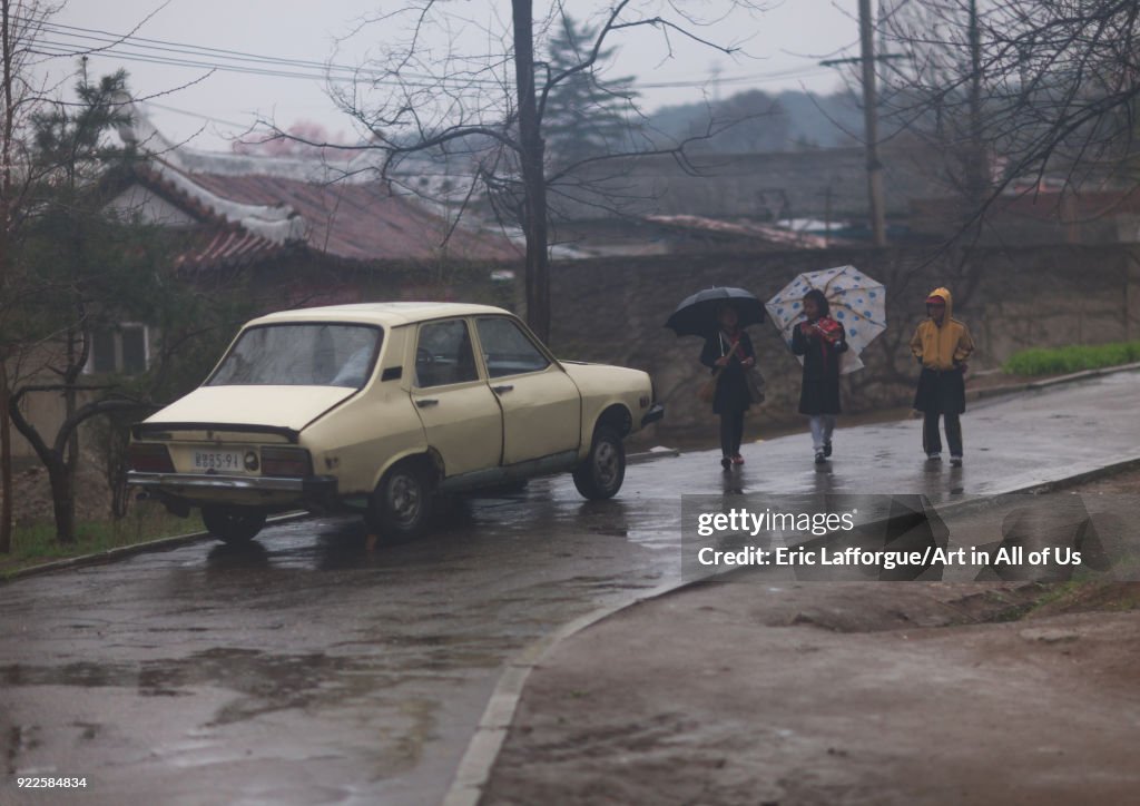 North Korean girls with umbrellas walking near a car under the rain, Pyongan Province, Pyongyang, North Korea...