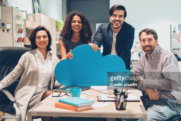 cheerful team of professionals holding a big blue cloud - cloud computing stock pictures, royalty-free photos & images