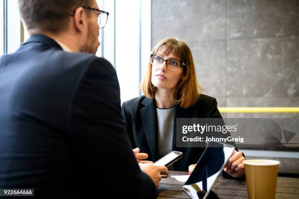 female manager discussing with male colleague using smartphone and tablet - wap stock pictures, royalty-free photos & images