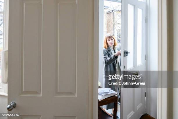 mid volwassen vrouw ontsluiten voordeur en thuiskomst - coming home door stockfoto's en -beelden