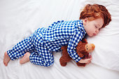 adorable redhead toddler baby sleeping with plush toy in flannel pajamas