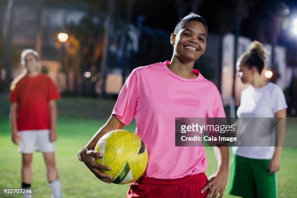Portrait confident, smiling young female soccer player with ball on field at night