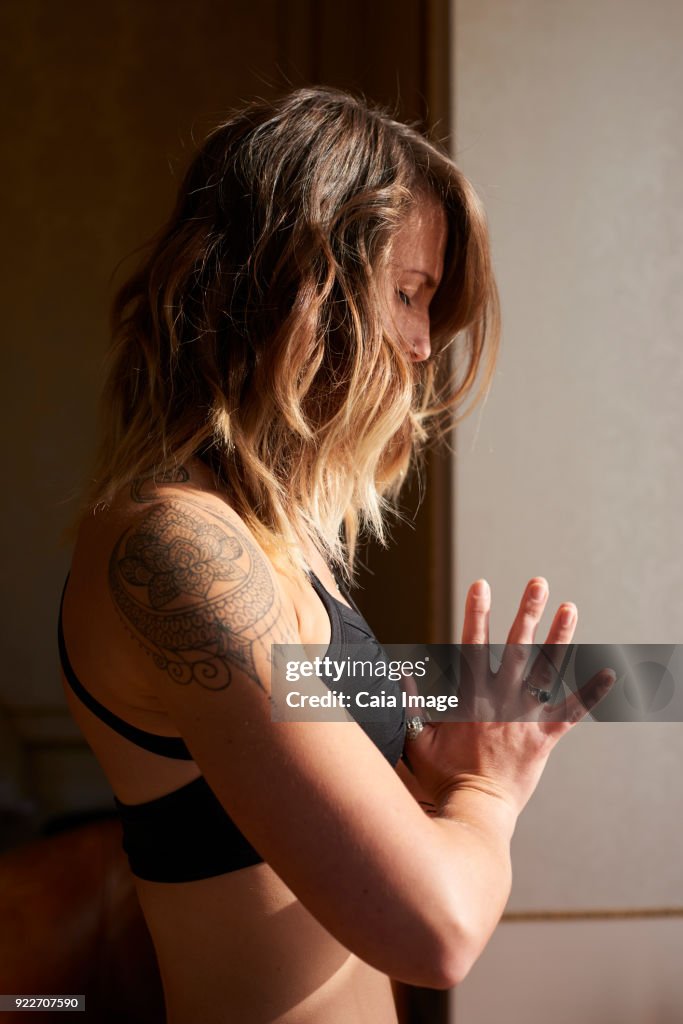 Serene woman with tattoo meditating with hands at heart center, anjali mudra