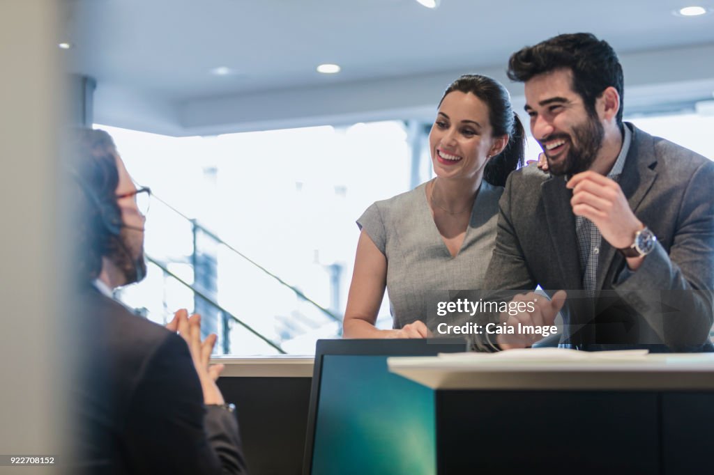 Smiling couple customers talking to receptionist at desk in car dealership