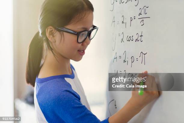 Portrait smiling, confident girl student solving physics equations at whiteboard in classroom