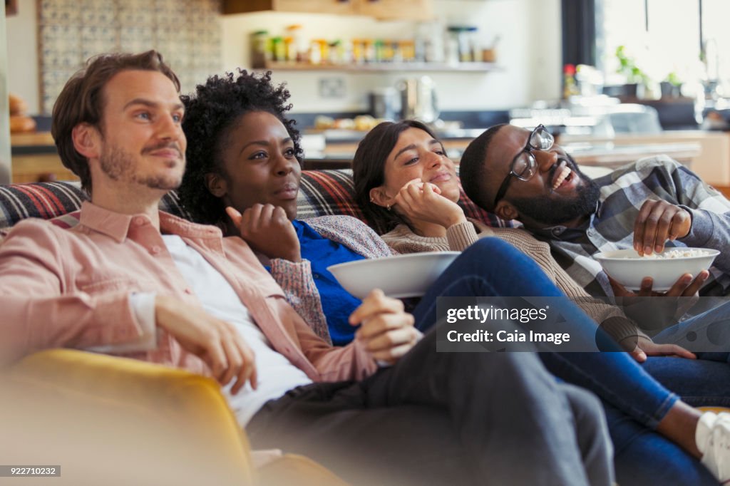 Couples watching TV and eating popcorn on living room sofa