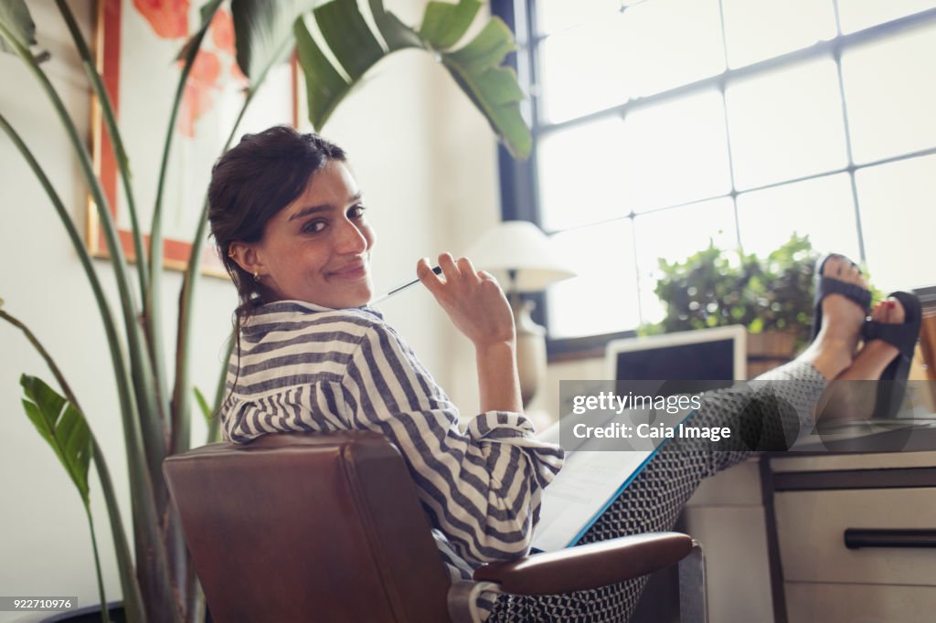 Portrait confident businesswoman working, reviewing paperwork with feet up on desk