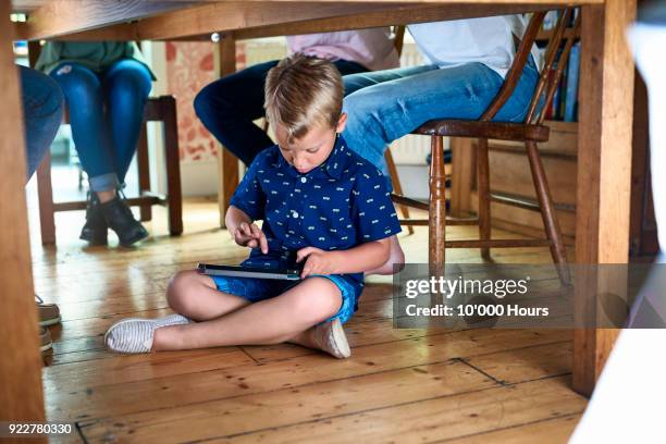 boy playing with digital tablet under table - legs on the table foto e immagini stock