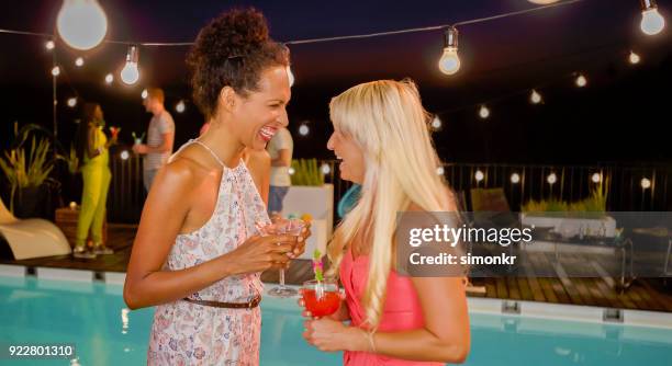 woman talking to female friend at party by pool at night - pool party night stock pictures, royalty-free photos & images