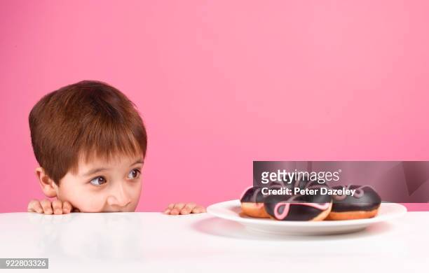 greedy boy looking at doughnuts - temptation stock-fotos und bilder