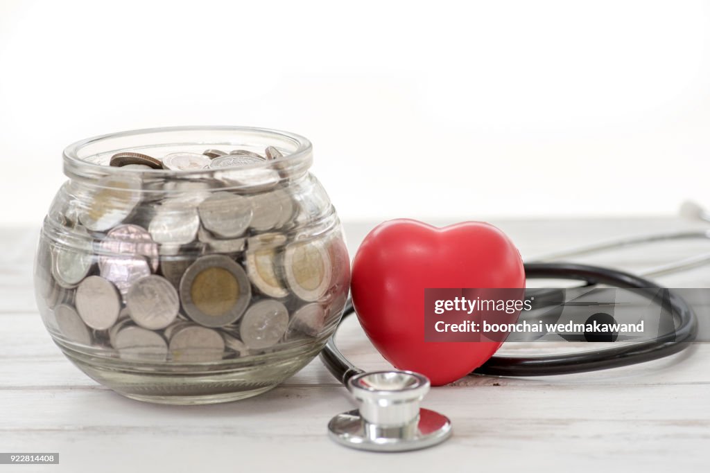 Close up stack of coins and hand holding red heart background, saving money for healthcare and manage for success business concept
