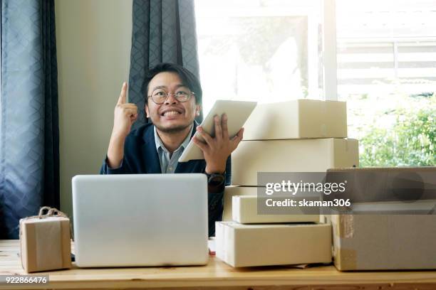 asian business man holding tablet for online shopping with laptop computer and with packaged to be shipped global - quitar fondo de imagen online fotografías e imágenes de stock
