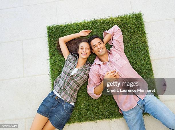 smiling young couple relaxing on a square of grass - lying on back photos - fotografias e filmes do acervo