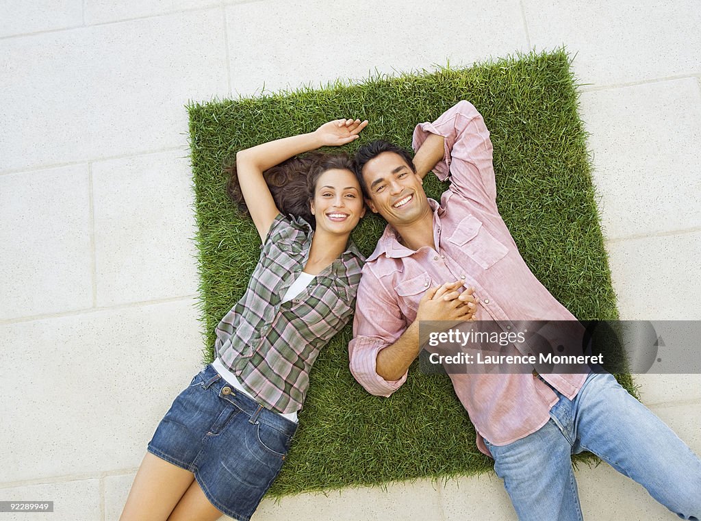 Smiling young couple relaxing on a square of grass