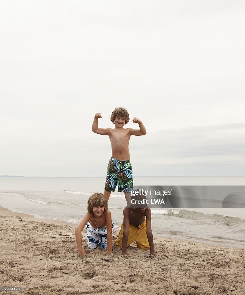Boy Standing On Friend's Backs, Flexing Muscles