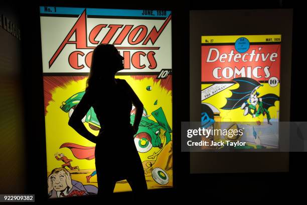 An employee poses in front illuminated displays of the first comics to feature Superman and Batman at the DC Comics Exhibition: Dawn Of Super Heroes...