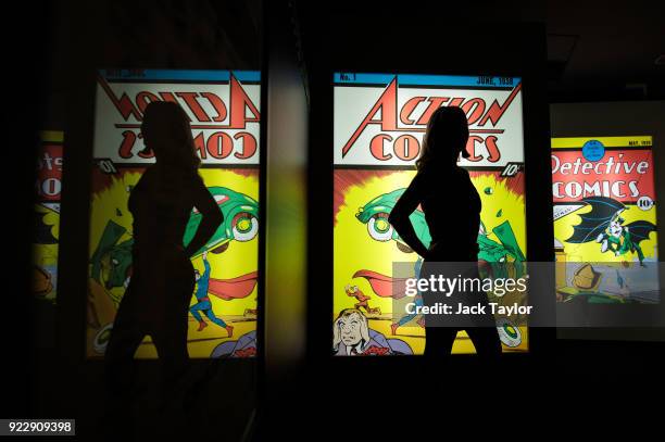 An employee poses in front illuminated displays of the first comics to feature Superman and Batman at the DC Comics Exhibition: Dawn Of Super Heroes...