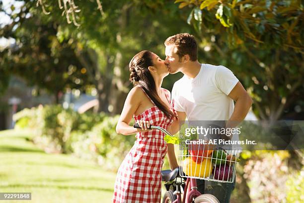 young couple kiss across bicycle - gingang stockfoto's en -beelden