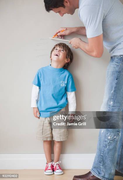 father measuring son's height against wall - height foto e immagini stock