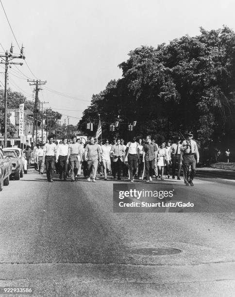 Group of student protests, escorted by a Sheriff's deputy, marches down a street carrying American flags and hippie peace symbol flags during an anti...