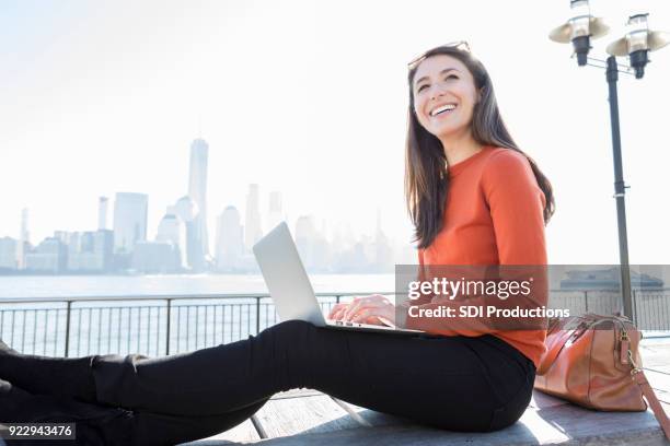 junge frau nutzt laptop, da sie auf new york city pier zurücklegt - bank student stock-fotos und bilder