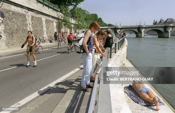 Une femme bronze, le 15 août 2001 sur la voie Georges Pompidou à Paris, tandis que des personnes à rollers et des cyclistes circulent sur ces quais...