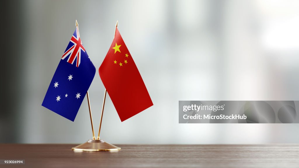 Australian And Chinese Flag Pair On A Desk Over Defocused Background