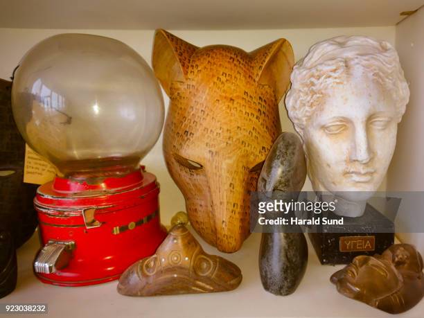 collection of a hand carved indigenous mask, gum-ball machine, abstract stone figure, aztec head and the bust of a hygeia, greek goddess of good health, displayed on a shelf. - aztec mask stockfoto's en -beelden