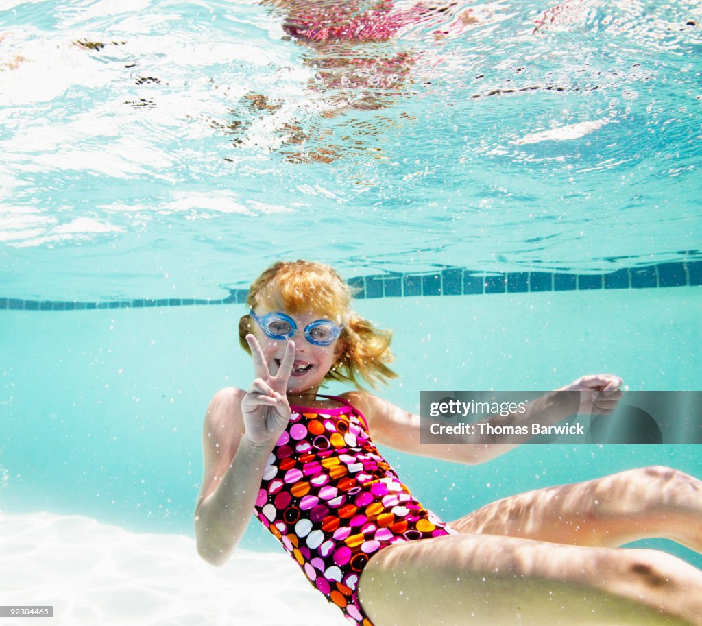 Young girl swimming in pool making peace sign