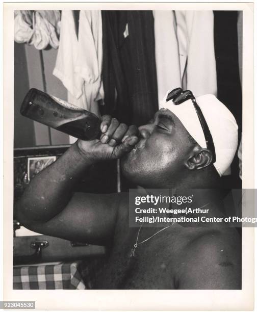 View of American Jazz musician Louis Armstrong , shirtless and with handkerchief on his head, as he drinks from a bottle backstage at the Basin...