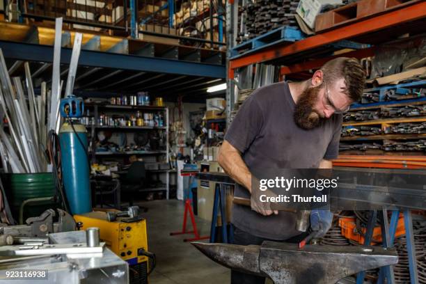 young artisan blacksmith using traditional anvil and forge - anvil stock pictures, royalty-free photos & images