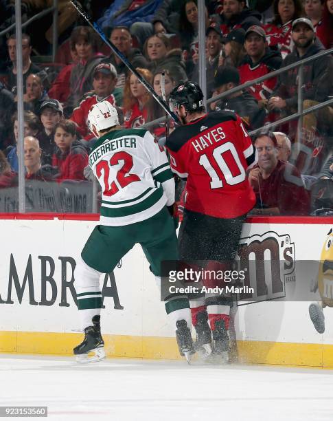 Jimmy Hayes of the New Jersey Devils is checked into the boards by Nino Niederreiter of the Minnesota Wild during the game at Prudential Center on...