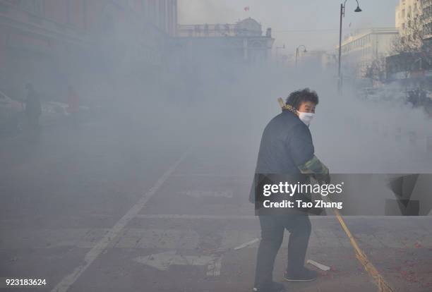 Woman cleans the street under heavy pollution as Chinese merchants set off firecrackers to pray for business boomingin front of a wholesale market on...