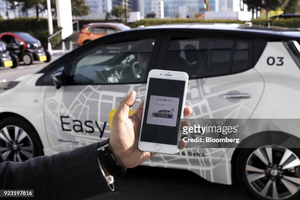 Smartphone screen displaying an arrival notification is arranged for a photograph in front of a Nissan Motor Co. Leaf electric vehicle during a...