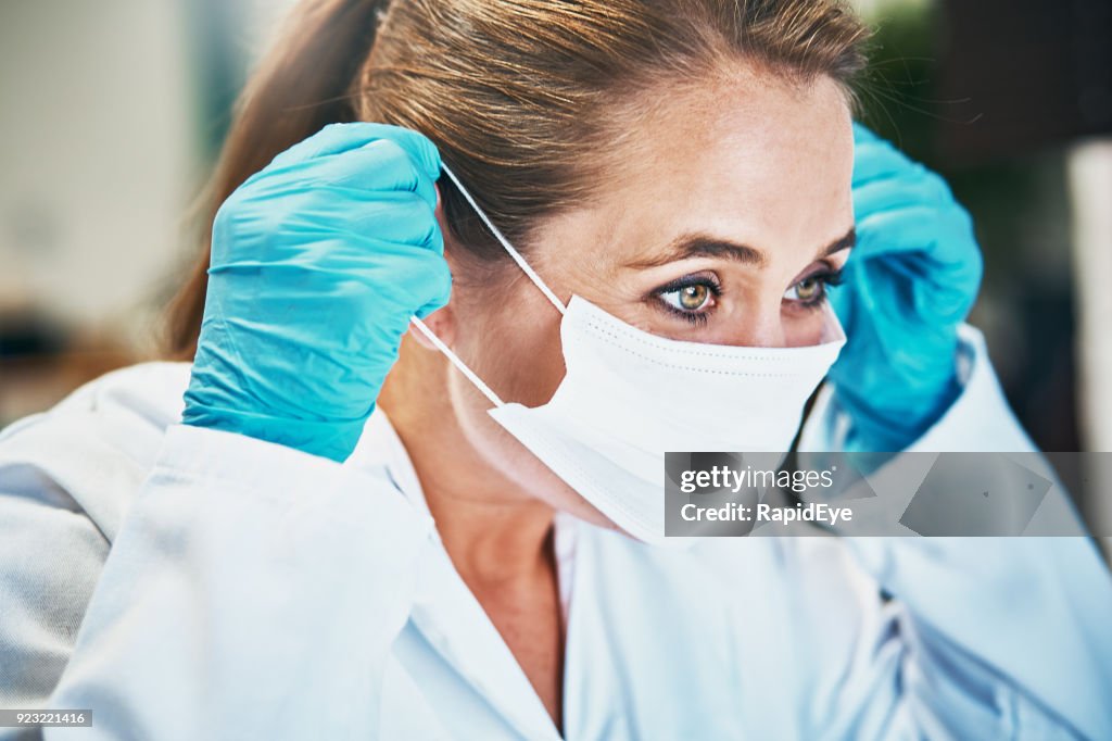 Woman scientist or medical professional putting on mask